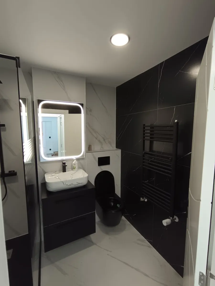 Baño reformado con mueble suspendido, espejo LED, inodoro suspendido y radiador toallero negro
