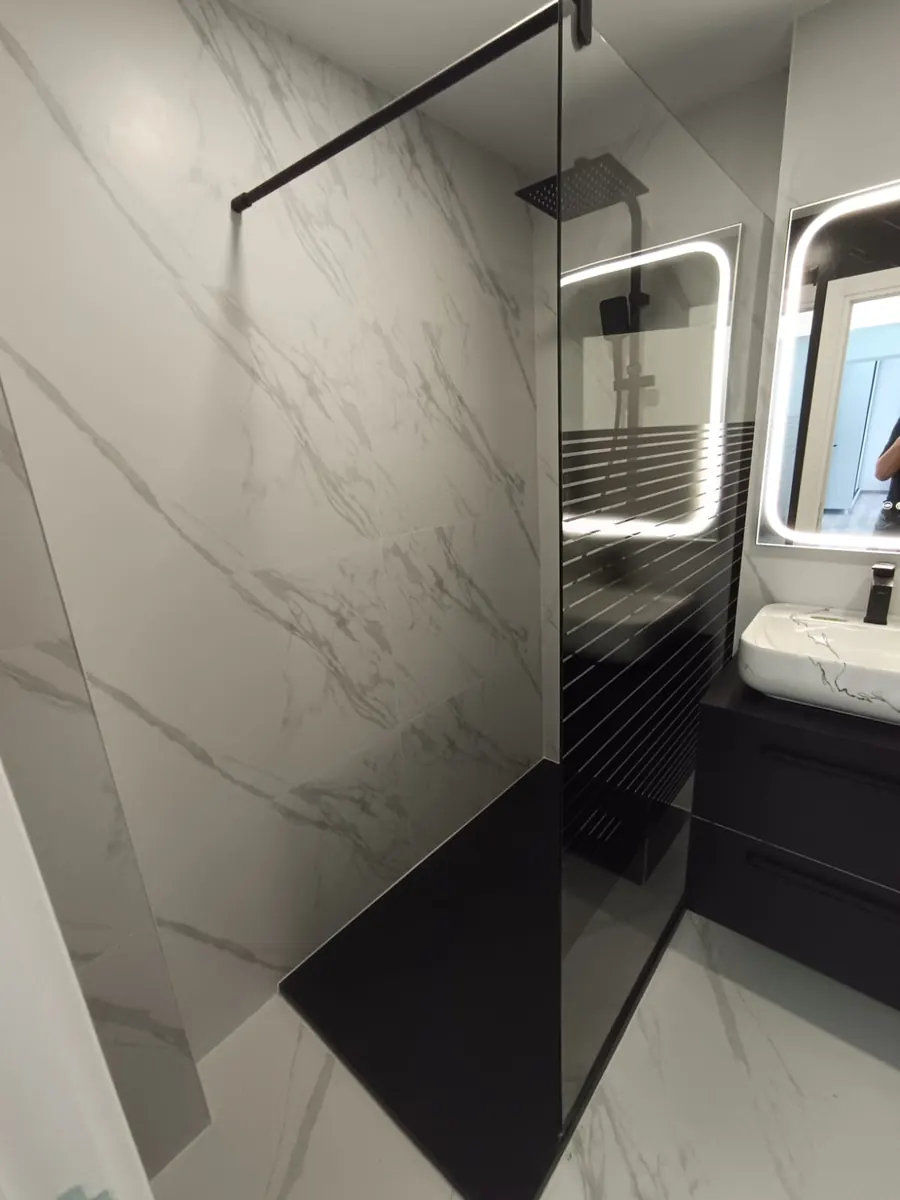 Ducha con mampara de cristal y porcelánico efecto mármol en un baño reformado por nuestro equipo